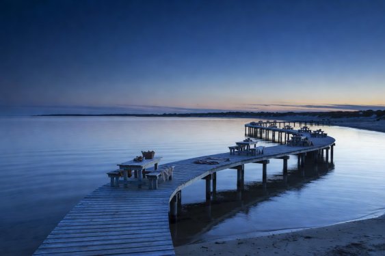 Wooden shoreline boardwalk curving along a tranquil bay at blue hour twilight
